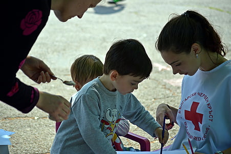 boy in gray long-sleeved shirt holding blue pencil beside woman in white and red crew-neck T-shirt during daytime