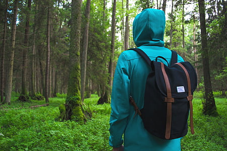 person wearing green hoodie and black backpack standing on forest during daytime photo