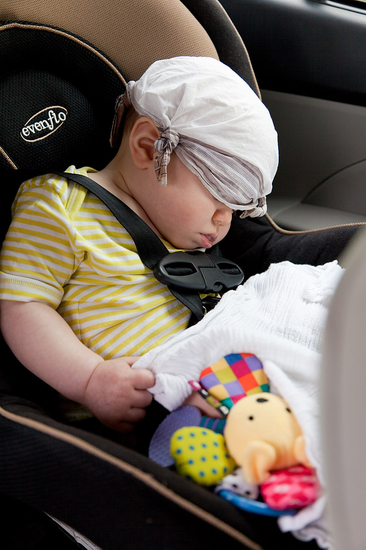 baby wearing yellow and white striped shirt sleeping on brown and black Evenflo booster seat inside car with white handkerchief covered on eyes and hair