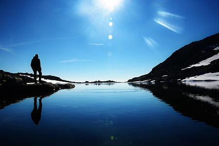 silhouette of man standing near body of water during daytime