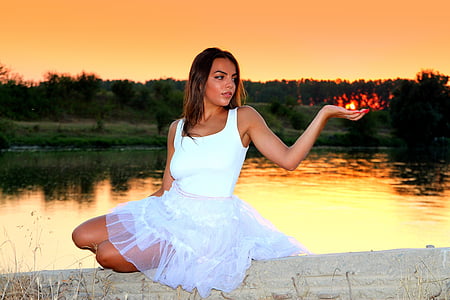 woman wearing white sleeveless dress sitting over lake during sunset