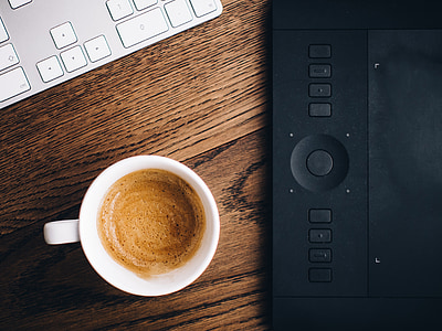 flat lay photography of white ceramic mug filled with coffee beside black graphics tablet