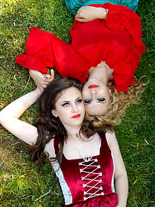 woman in maroon dress beside woman in red top lying on green grass