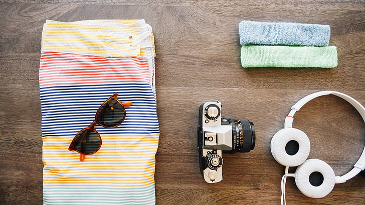 flat lay photography of camera, headphones, sunglasses, and board shorts