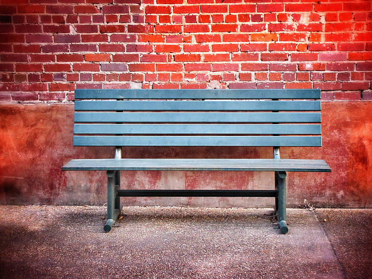 Royalty-Free photo: Black wooden bench against red brick wall | PickPik