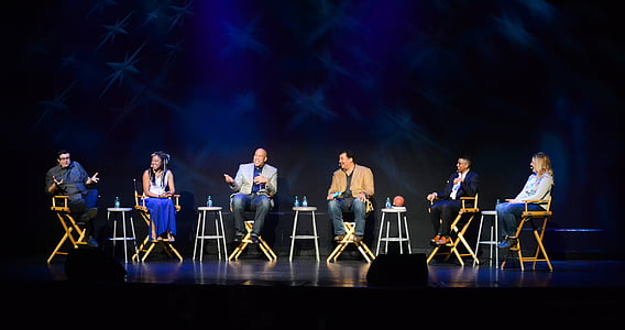 six people sitting on chairs on stage