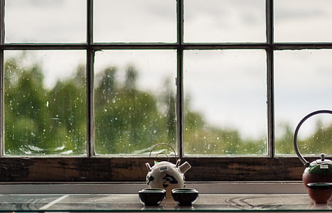 white ceramic teapot with two cups infront of the window