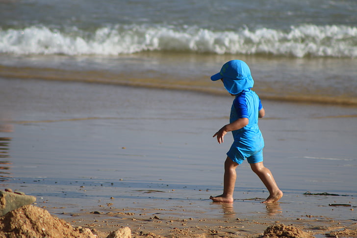 toddler wearing blue shirt walking on shore near sea