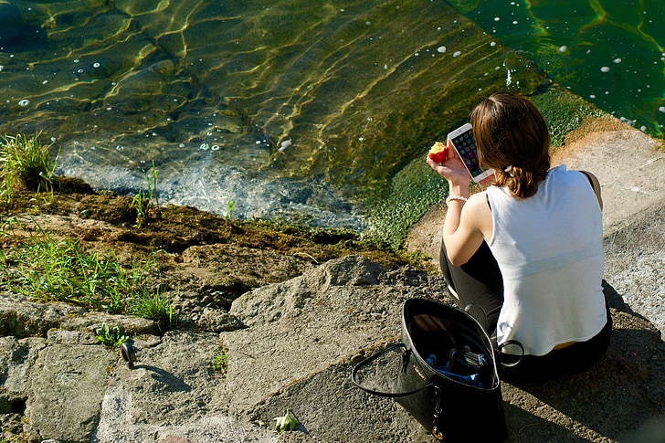 woman using smartphone beside body of water