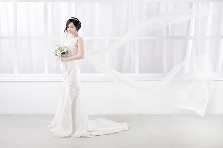 woman standing wearing white wedding gown holding flower bouquet