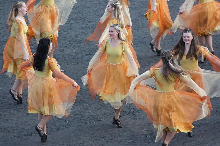 group of women wearing yellow and orange dresses dancing together