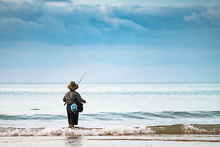 person standing on seashore holding fishing rod