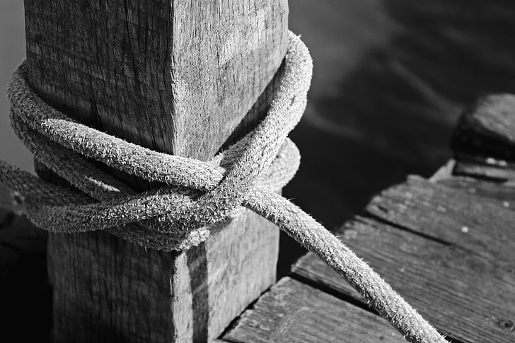 grayscale photo of tied rope on lumber