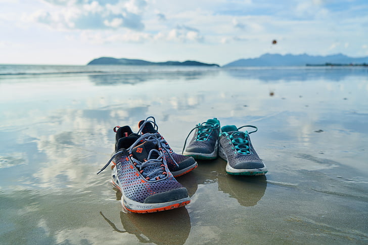 two pairs of athletic shoes on grey sand beach shore