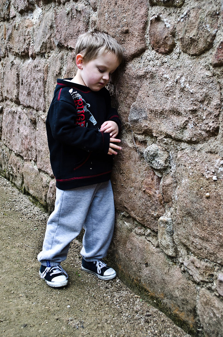 boy leaning on brown concrete wall