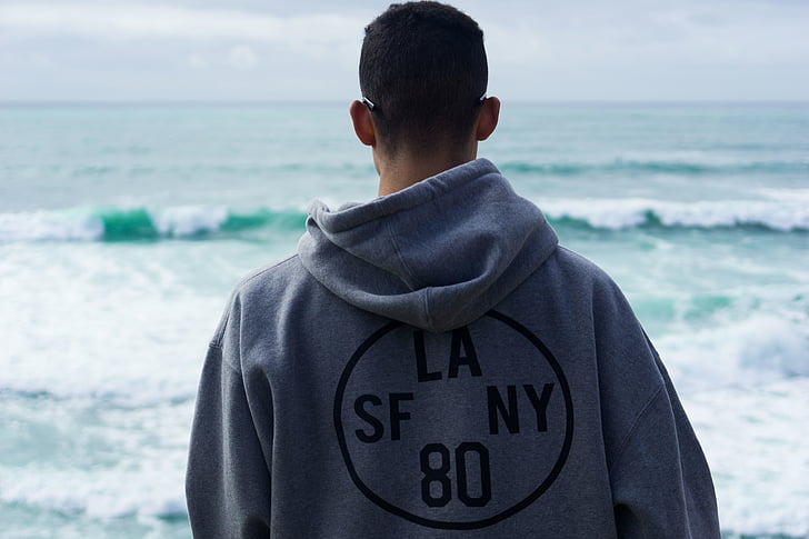 man wearing gray LA SF NY 80 hooded jacket standing near sea during daytime