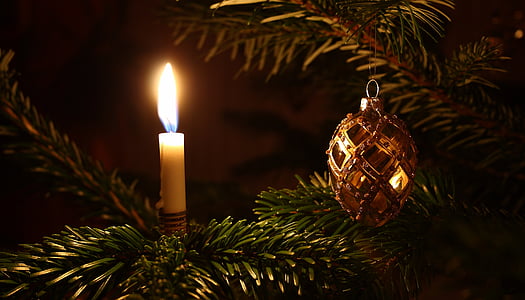 lighted taper candle beside Christmas ornament hanging on fir tree