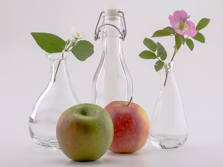 two apple fruits beside three glass bottles