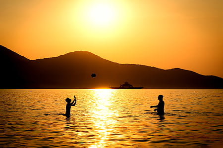 silhouette of two people playing ball on water during sunset