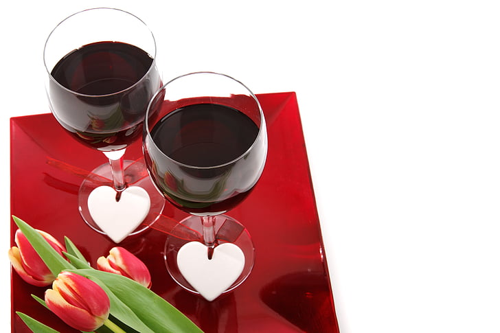two wine glass with red wine inside beside tulip flowers