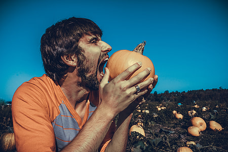 man wearing orange crew-neck shirt eating orange pumpkin during daytime photo