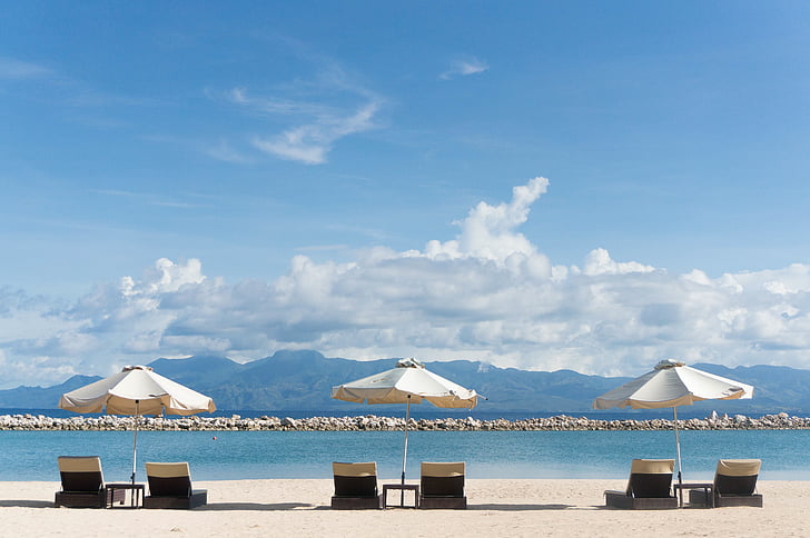 three white patio umbrella on black coffee tables with six fainting lounges near seashore