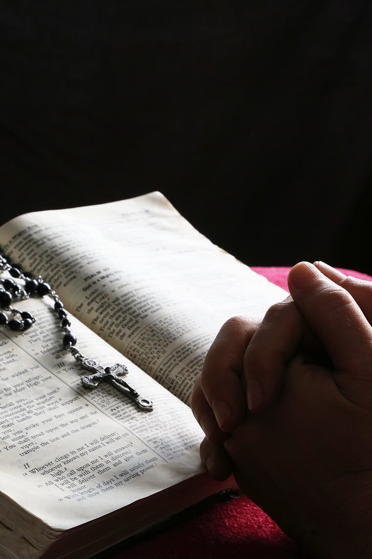 person praying in front of the rosary and bible