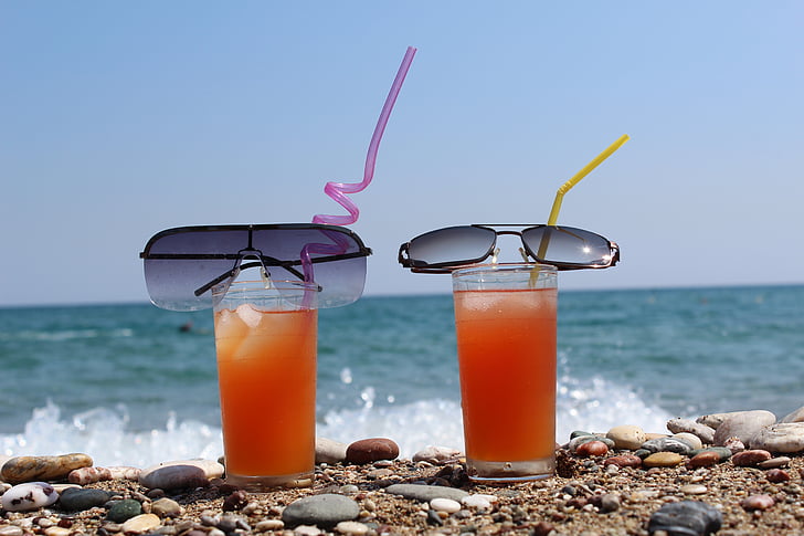 two black sunglasses on top on clear drinking glasses filled with orange liquid on the beach during daytime