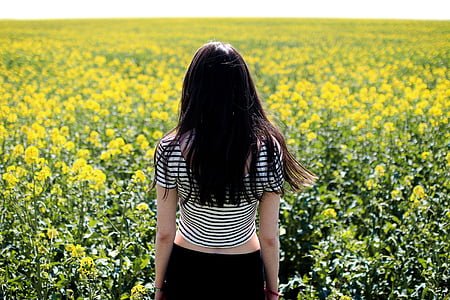 woman wearing white and black striped t-shirt surrounded by yellow petaled flower at daytime