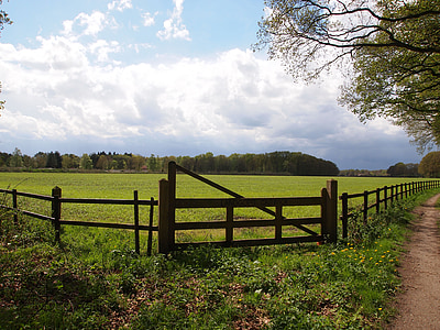 green field surrounded by brown wooden fence under white clouds and blue sky