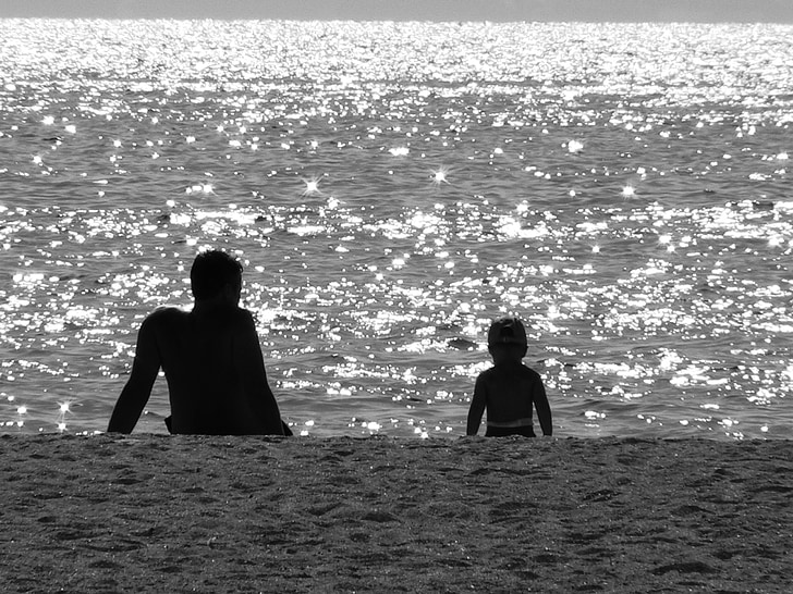 silhouette of man and child facing seashore during daytime