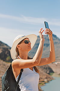 woman in white tank top holding black iPhone during daytime