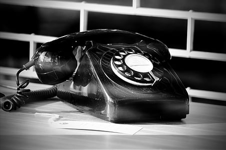 grayscale photography of rotary telephone near white metal window grille
