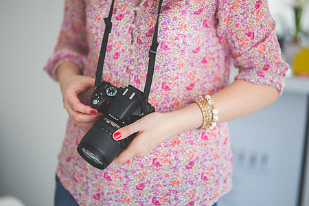 person wearing red floral shirt holding black DSLR camera
