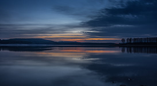 calm body of water near gray clouds during sunset