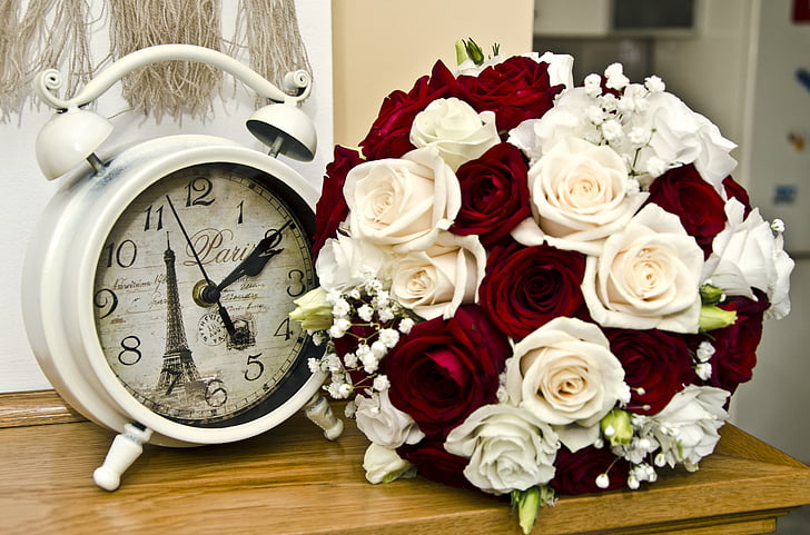round white Paris analog alarm clock and bouquet of red and white flowers on brown wooden table