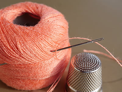silver thimble beside orange thread with needle