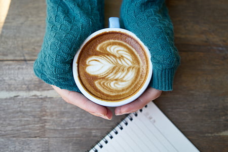 person holding cup with coffee art