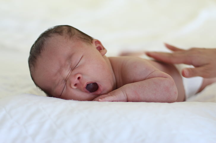 yawning baby lying on white textile