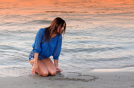 woman in blue elbow sleeved shirt kneeling on beach during sunset