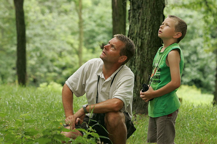 man wearing white polo shirt with boy wearing green tank top looking at the trees during daytime