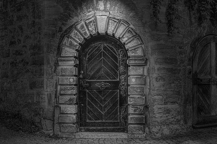 grayscale photo of arch-shaped black wooden panel door