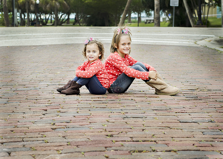 two girls in red polka dot sweater sitting on paver bricks