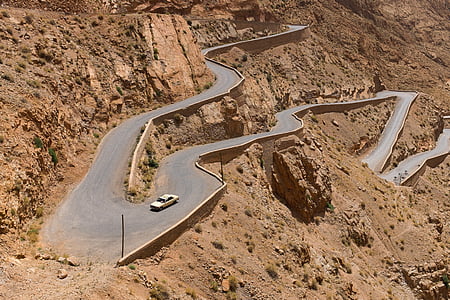 white car traveling on a narrow curve roads at daytime