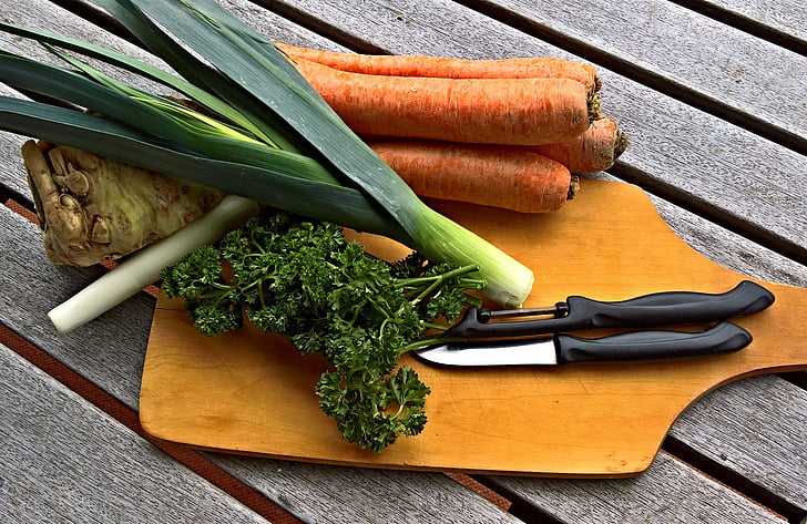 carrots and spring onions with knife on brown chopping board