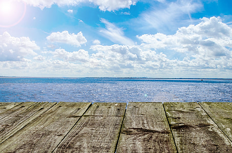 brown dock beside calm sea under white cloud blue skies