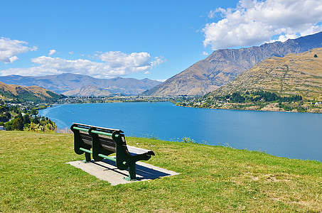 brown wooden bench near body of water and mountain peak