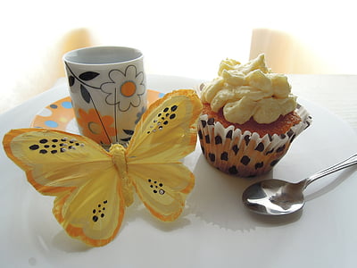 cupcake, silver spoon, ceramic mug, and yellow butterfly decor on table