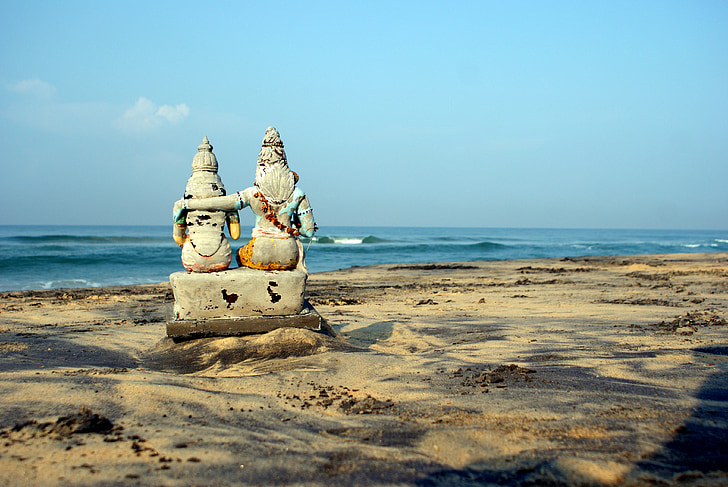 two deity statuette on seashore at daytime