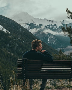 man seats on bench near mountains